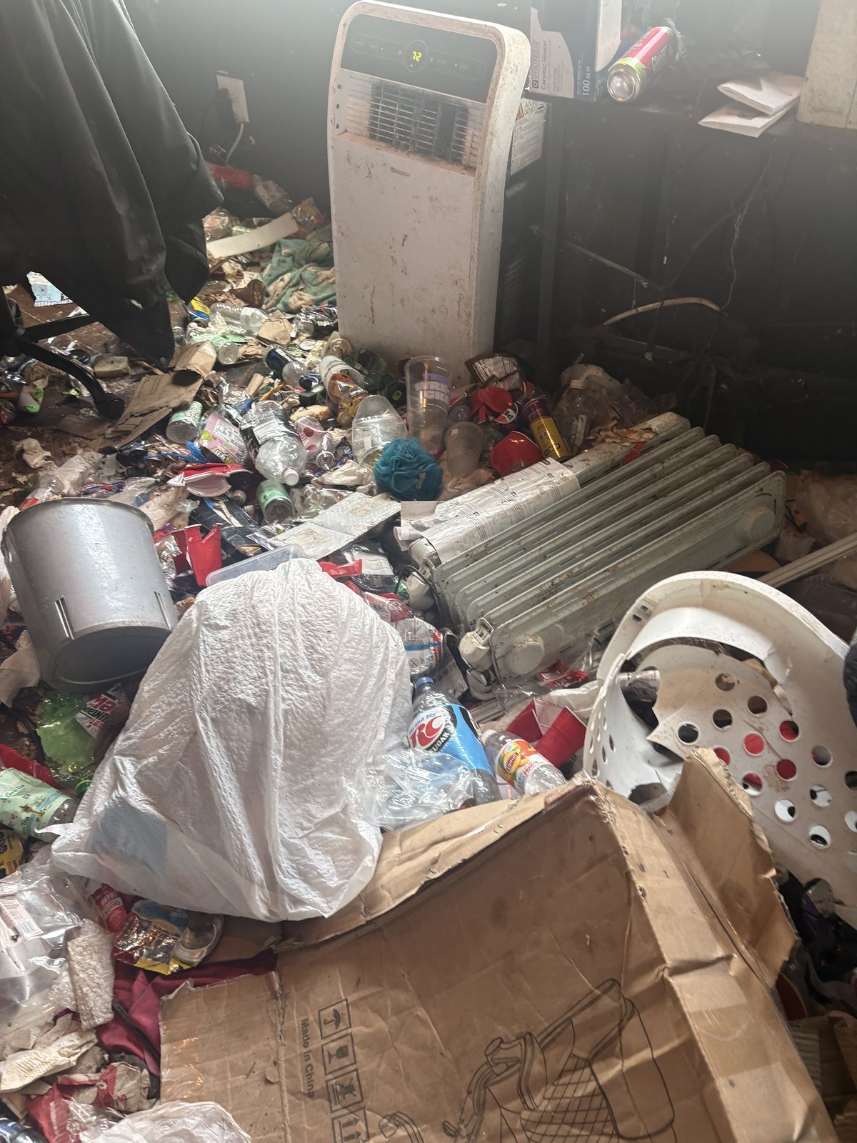 Before: Back room floor buried knee-deep in bottles, cans, bags and boxes around a portable AC unit